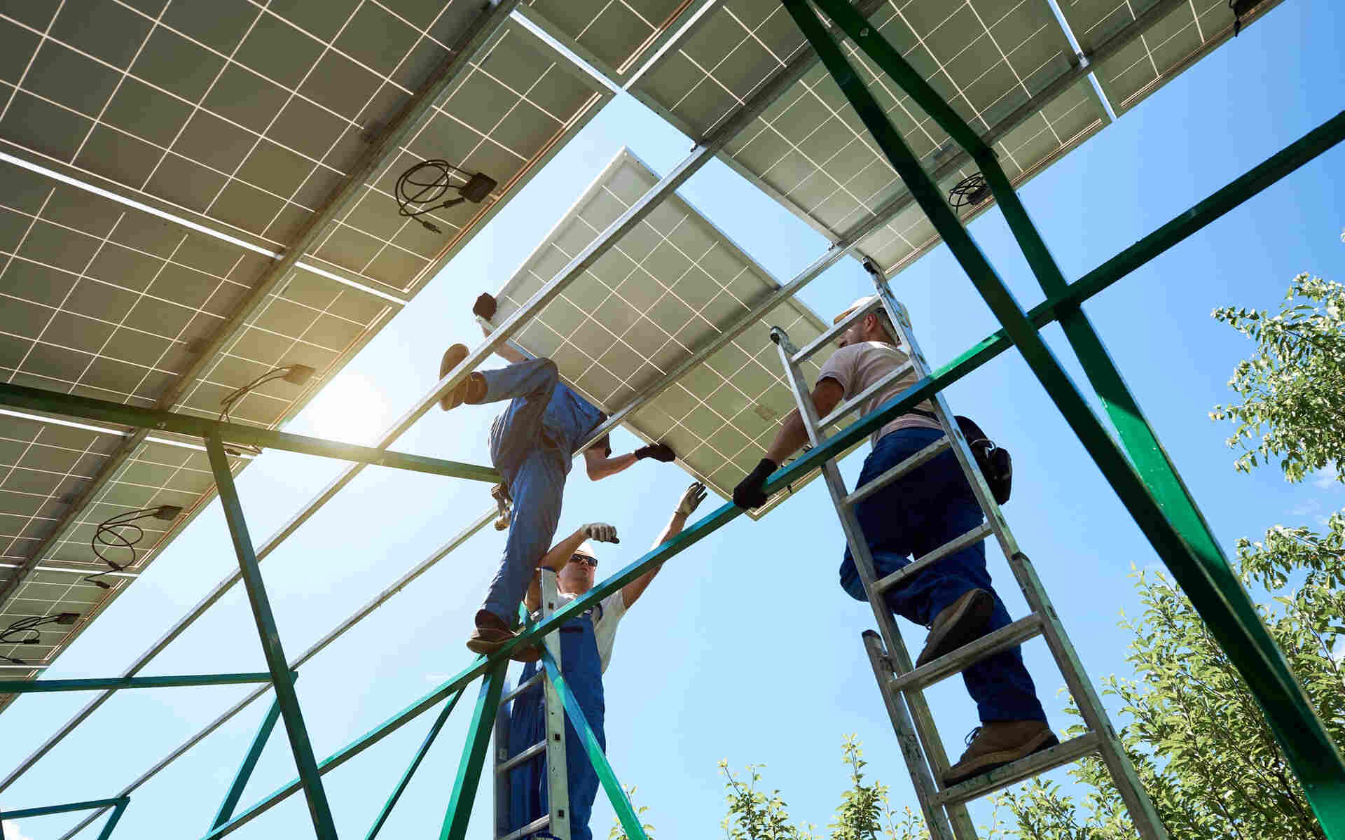 Technicians working on a commercial solar panel installation structure under clear blue skies.