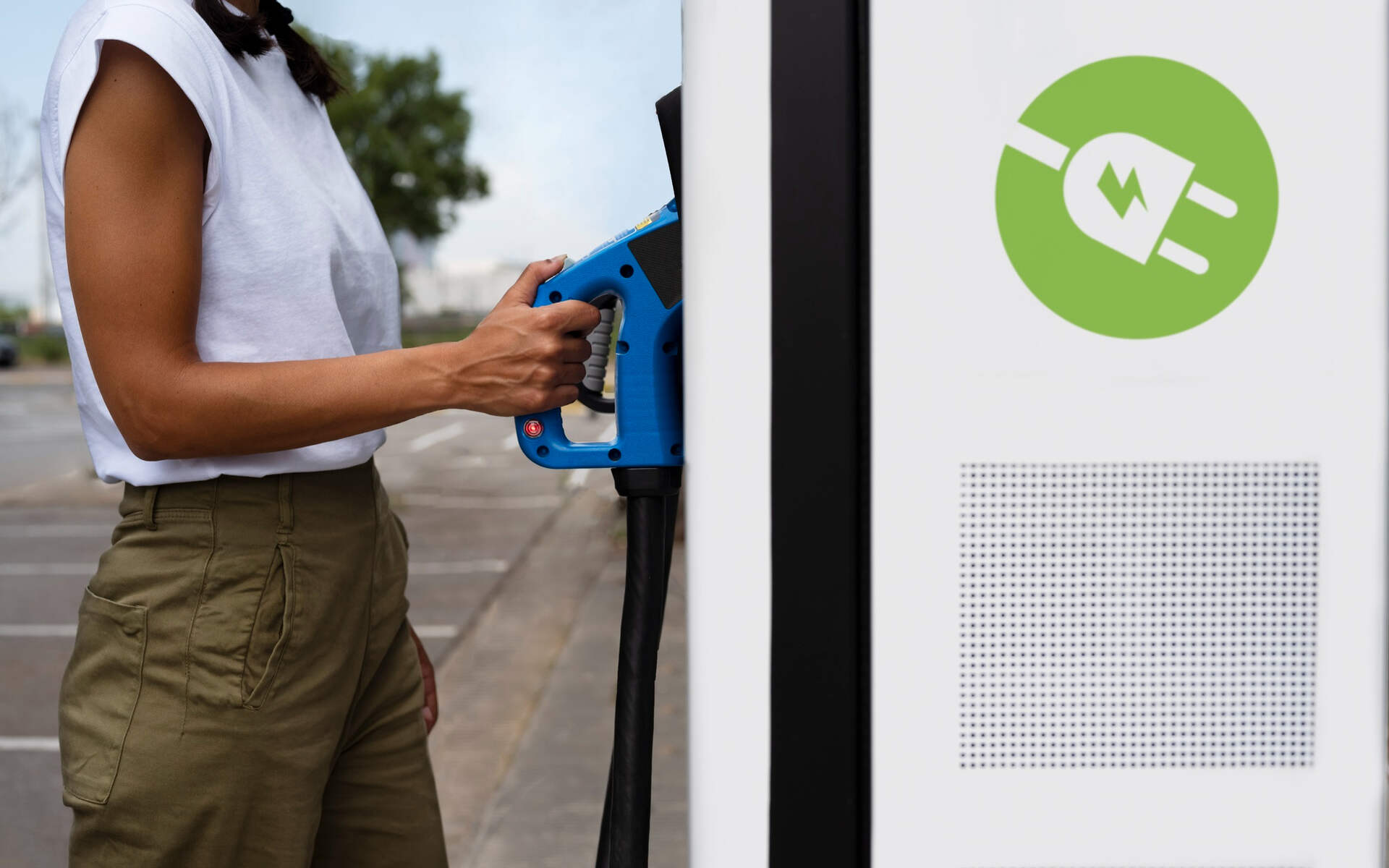 A woman connects a cable to an electric vehicle charging station, showcasing the best EV charger in action.