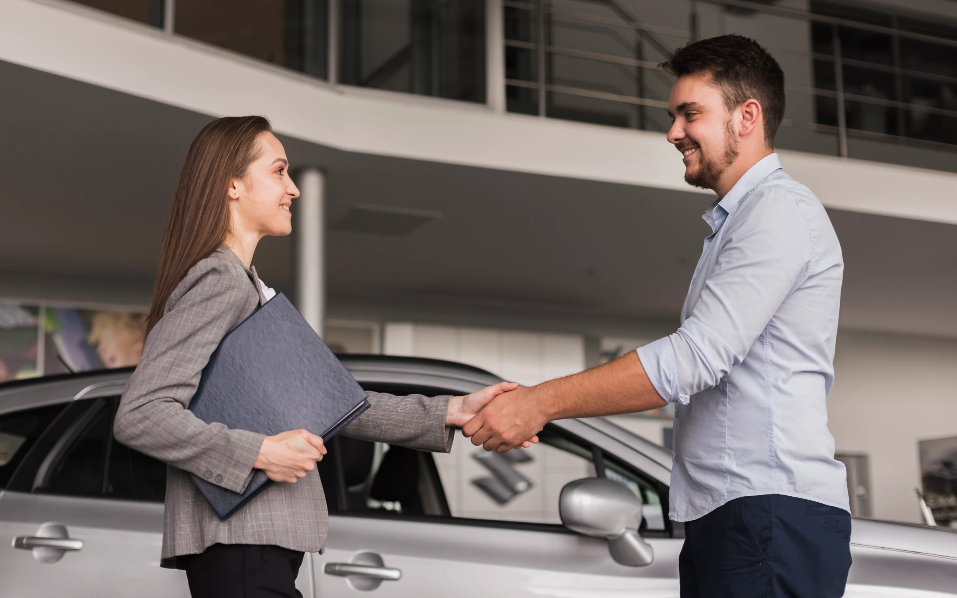 A man and a woman are shaking hands in front of a silver car, likely finalizing a purchase or lease under the Charge Up New Jersey program.