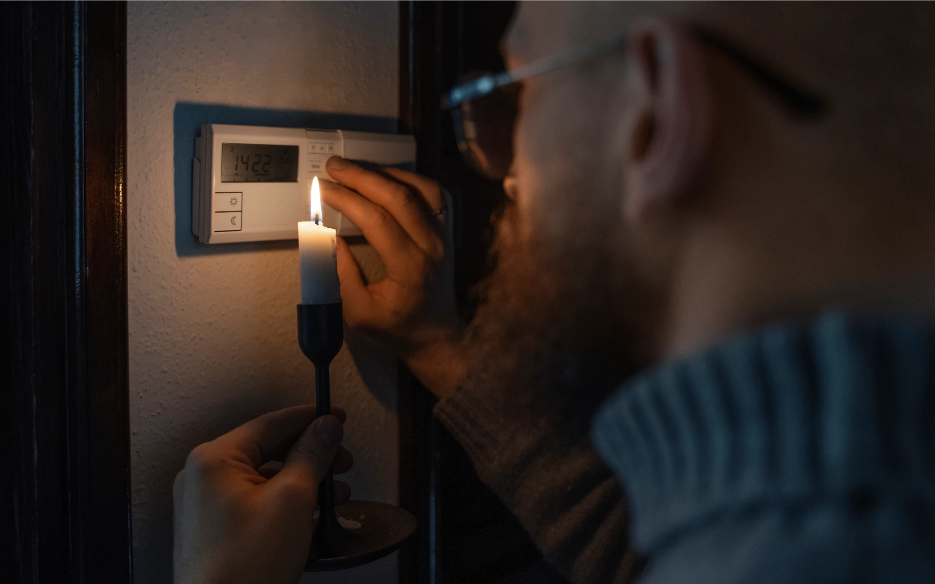 A person adjusts a thermostat by candlelight during a power outage, emphasizing the importance of having a backup generator in New Jersey.