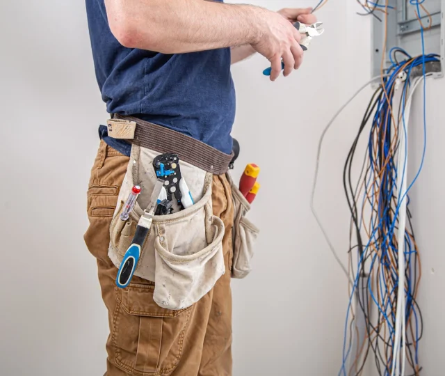 electrician-builder-work-examines-cable-connection-electrical-line-fuselage-industrial-switchboard-professional-overalls-with-electrician-s-tool